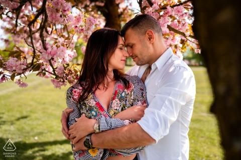Under a cherry tree in Slovenia, a couple hugs, framed by the tree’s branches and soft natural light, capturing a simple, intimate portrait in a peaceful outdoor setting.