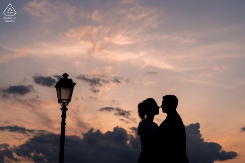 In Trieste, Italy, a silhouette of a couple stands against the vibrant sky, their forms outlined by the golden light of sunset, creating a dramatic and intimate portrait of their bond.