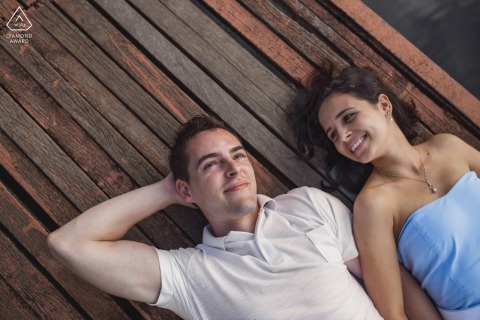 On a deck at Praia do Francês in Alagoas, Brazil, two lovers lie back on wood dock, smiling as they look up at the sky.