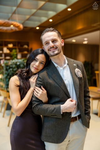 Inside the modern and stylish Aigu Restaurant & Bar in Zoug, Switzerland, the couple stands side by side, with the bride-to-be gently holding his arm during their professional indoor session.