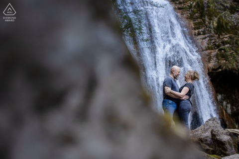Stunning Pre-Wedding Portrait Highlights Romance Amidst A Scenic Waterfall In Saint Vincent De Mercuze France This stunning pre-wedding portrait features the couple positioned near a scenic waterfall in Saint Vincent de Mercuze, France, highlighting their romance amidst the lush greenery and flowing water.