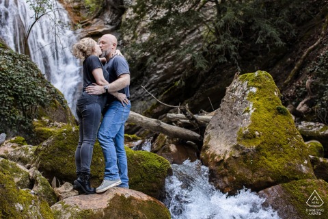 Two Lovers Embrace The Natural Beauty And Powerful Energy Of A Rushing Waterfall In France Standing before a majestic, rushing waterfall in Saint Vincent de Mercuze, France, the two lovers embrace the natural beauty and powerful energy of the French landscape for their portraits.