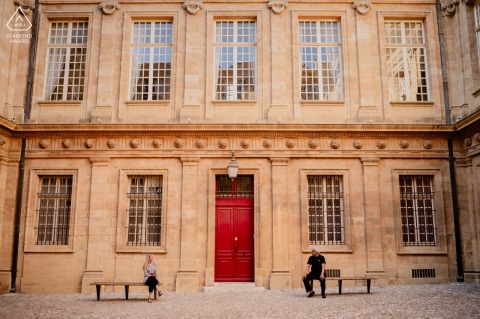 In Aix En Provence The Photographer Places The Couple On Separate Benches For Stylish Symmetry In the city center of Aix en Provence, the couple shares a stylish engagement portrait on separate benches amid historic streets, soft light, and the old world rhythm of the city.