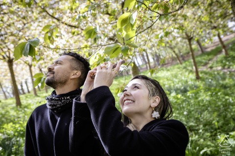 At The Alnwick Garden in Alnwick, Northumberland, UK, a newly engaged couple enjoys a playful touristy portrait surrounded by lush gardens and relaxed, cheerful energy.