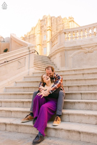 In Dubrovnik Croatia The Seated Couple Poses At Sunset With Warm Historic Surroundings In Dubrovnik, Croatia, the seated couple poses on the steps at sunset during their engagement session, sharing a calm portrait with warm colors, historic surroundings, and gentle intimacy.