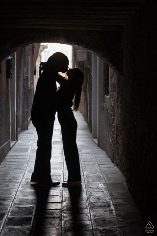In A Romantic Venice Alley The Silhouetted Couple Poses Close Against Dreamy Historic Shadows In a romantic alley in Venice, a silhouetted couple stands close together, their outlines softened by the historic setting and the city’s dreamy atmosphere.
