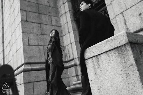 On the Bund in Shanghai, China, the couple stands against a grand stone façade in black and white, styled like a classic film frame with quiet drama.