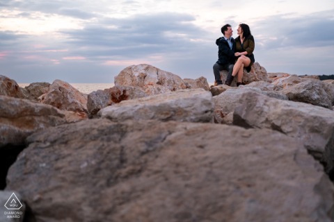 On the rocks of a pier in Croatia, the couple sits close together, sharing a calm coastal portrait with weathered stone textures and a quiet, intimate atmosphere.