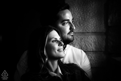 In Jaén, Andalucía, Spain, a black-and-white pre-wedding portrait shows the couple in profile, both looking out toward window light with quiet intensity and timeless elegance.