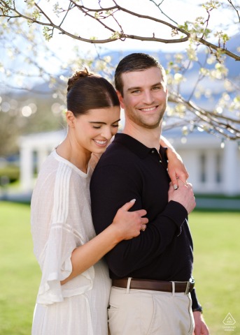 Pre-wedding engagement portrait of a smiling couple embracing beneath spring blossoms at the Equinox Resort in Manchester, Vermont.