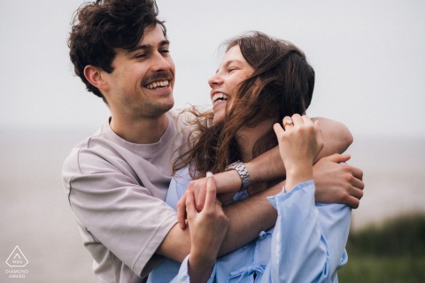 A joyful couple embraces and laughs together during a romantic pre-wedding portrait session in Meschers-sur-Gironde, France.