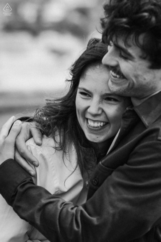 An engaged couple hugs closely and smiles together during a black and white pre-wedding portrait session in Meschers-sur-Gironde, France.