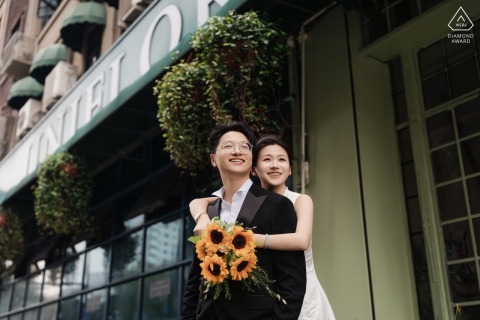 The future bride wraps her arms around her fiancé outside a landmark building during their engagement session at the Bund in Shanghai, China.