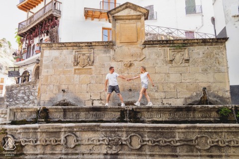 The Couple Walk Beside An Old Stone Wall In Cazorla, Jaén, Spain A couple walks hand in hand along an old stone wall in Cazorla, Jaén, Spain, during a scenic pre-wedding engagement photo session.