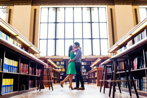A couple poses in the center of the university library during a pre-wedding engagement session at UC Berkeley in California, surrounded by bookshelves.