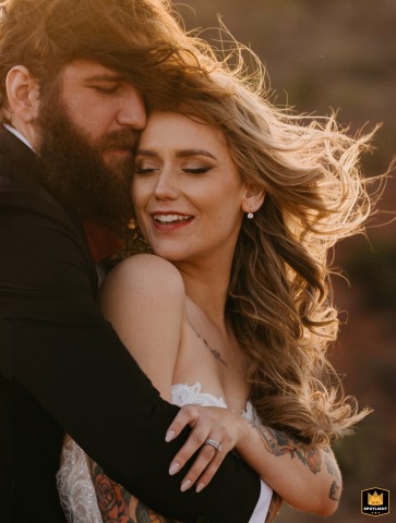 In Sedona, Arizona, a groom lovingly embraces his bride in a post-ceremony portrait, with the sun creating a beautiful halo effect on their blending, windswept hair.
