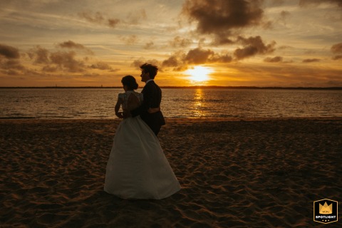 Sunset Stroll: Newlyweds Savor Quiet Moment at Arcachon Wedding Venue A romantic scene at Arcachon, France - the newlyweds take a peaceful 10-minute break by the sea, strolling hand in hand as the sun shrinks in size at the horizon before their seaside dinner.
