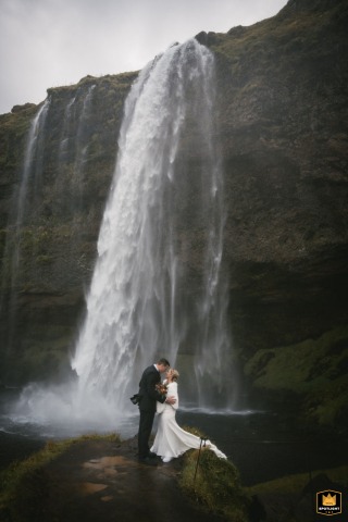A WPJA wedding photo: A dramatic, tall vertical shot shows a couple kissing in front of a large waterfall on Iceland's south coast.