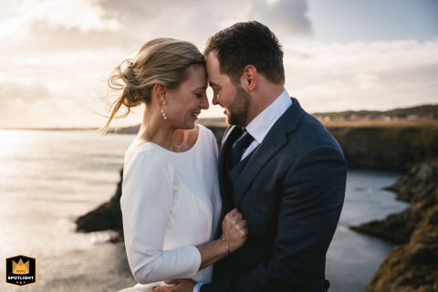 On the Snaefellsnes peninsula, Iceland, the couple hugs head-to-head on the cliffs over the sea, in the wind at sunset.