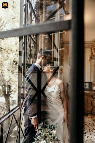 At City Council, Forlì, Italy, the bride and groom share a candid kiss behind an ancient window.
