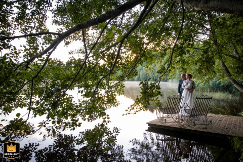A WPJA wedding photo: The couple stands on a wooden dock by Lac de Chamboux, enjoying the calm water and surrounding trees.