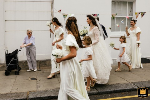At Chelsea Physic Garden, London, the wedding party, dressed in white, walks through a street scene, encountering a surprised elderly lady.