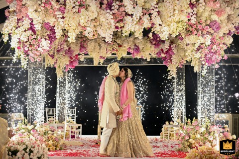 At JW Marriott, Phuket, the couple shares their first kiss after the wedding, framed by massive soft pastel flowers above them.