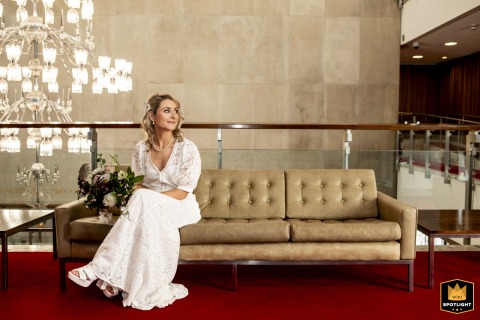 At Newcastle Civic Centre, UK, the bride sits alone on a lobby couch, waiting for her husband to finish talking.