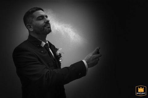 At a hotel room in Zug, Switzerland, a groom sprays cologne in a dramatic black and white shot, captured by a WPJA photographer.