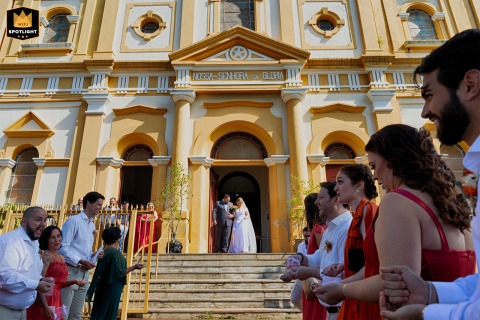 Bride and groom exit Paróquia Nossa Senhora da Glória in Porto Alegre as excited guests eagerly wait to celebrate outside.