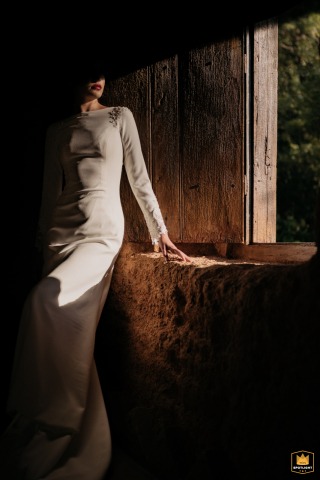 A WPJA wedding photo: In São Paulo, a bride in a white dress sits on an indoor stone windowsill, sun highlighting her mouth downwards.