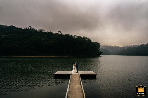 In São Paulo, a couple stands alone at the end of a small wooded boat dock, beneath storm clouds over calm, flat water.