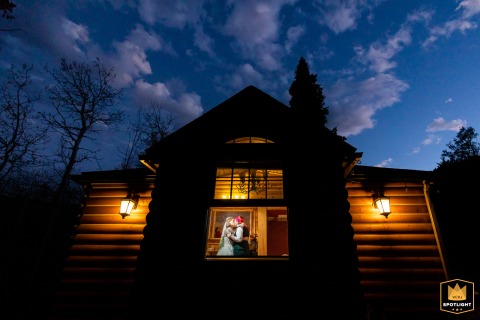 A WPJA wedding photo: At dusk in Rocky Mountain National Park, Colorado, newlyweds kiss inside their cabin, framed by silhouetted trees and the sky.