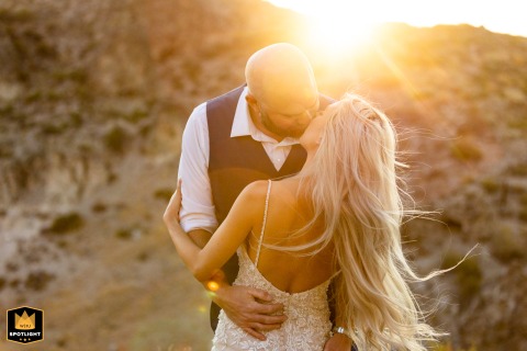 In Hot Springs, Mammoth Lakes California, the groom gives his bride a romantic kiss, her hair blowing in the warm, glowing sunset breeze.