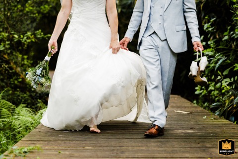 At a private reception venue in Messanges, France, newlyweds walk barefoot, laughing and holding their shoes, a joyful detail.