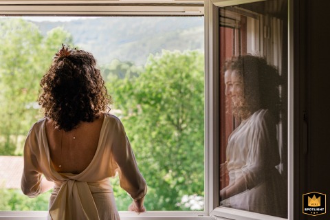 Bride framed by a window in the Pays Basque countryside, gazing outside in peaceful solitude before the wedding ceremony.