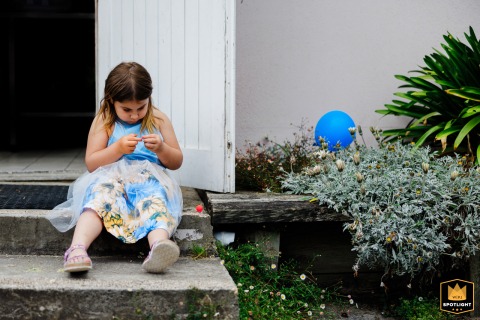 A flower girl sits thoughtfully with a blue balloon outside the Pyrénées-Atlantiques wedding venue.