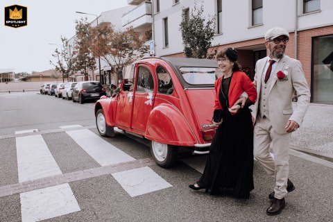 In front of Mondonville town hall, groom and his mother cross the street behind a red Citroën 2CV, approaching guests.