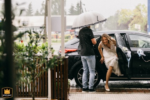 Bride steps out of car at a West Pomeranian, Poland, hotel after waiting for heavy rain to stop on wedding day.