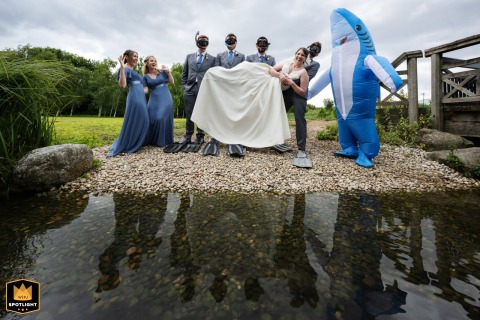 Wedding party poses in river at London Wetland Centre, creating a stunning group reflection on the water’s calm surface.