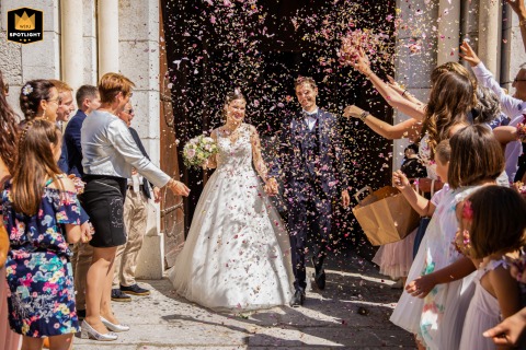 Bride and groom exit Le Touvet Church, Isère, France, smiling and holding hands as they step outside after their ceremony.