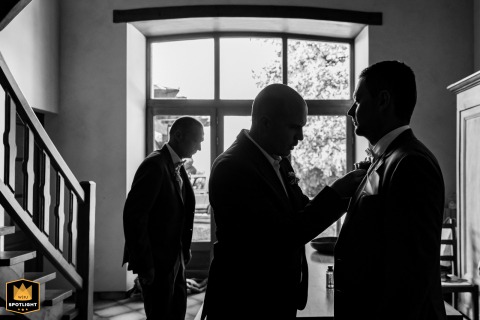In Nances, Savoie, France, groom stands in his home, receiving assistance with his tie while preparing for the wedding.