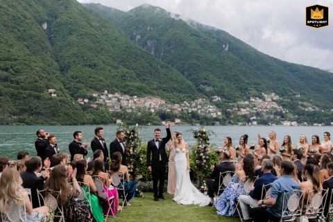 Bride and groom joyfully clasp hands and raise arms at Villa Regina Teodolinda altar, Lake Como, celebrating their wedding ceremony.