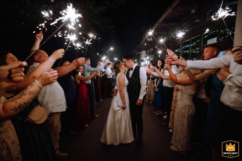 Bride and groom kiss at night in Budapest, walking through a tunnel of guests holding sparklers, creating a magical farewell.
