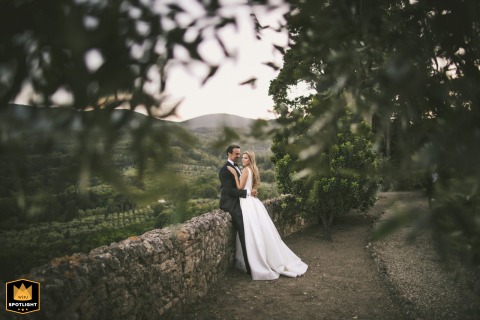 At Rocca di Cetona in Tuscany, the couple shares a relaxed portrait as they lean on a long, low stone wall, surrounded by the picturesque countryside's rolling hills and timeless beauty.