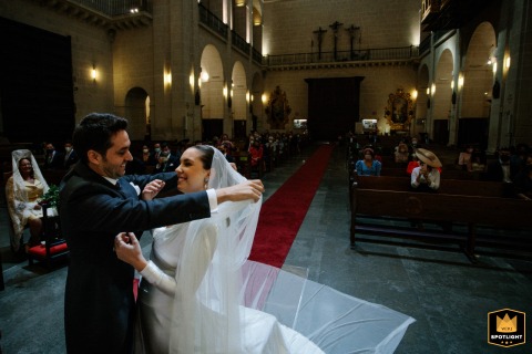At Alicante Cathedral in Spain, the groom gently removes the bride’s veil during the wedding ceremony, capturing a poignant and intimate moment of love and anticipation before they are pronounced husband and wife.