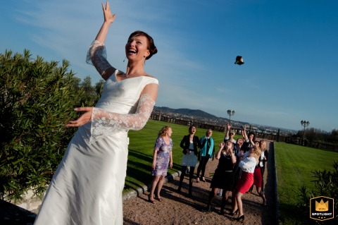 At Villa Malliana in Almenno San Bartolomeo, Bergamo, Italy, the bride joyfully tosses her bouquet under a vivid blue sky. Surrounded by enthusiastic friends, the moment radiates excitement, fun, and anticipation during this beloved wedding tradition.