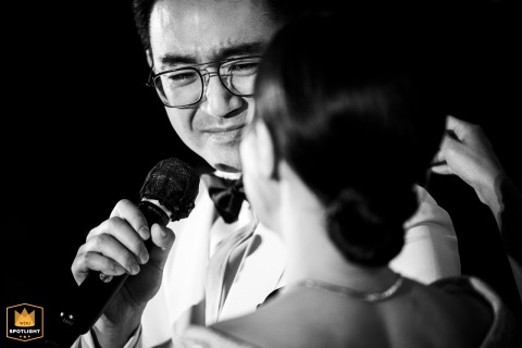 At Grand Hyatt Erawan, an emotional black and white close-up captures the groom speaking into a microphone, his gaze fixed tenderly on the bride. 