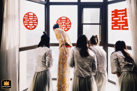 In Kaifeng, China, the bride and bridesmaids look down through a window, anticipating the groom's arrival. The scene captures a moment of excited waiting.