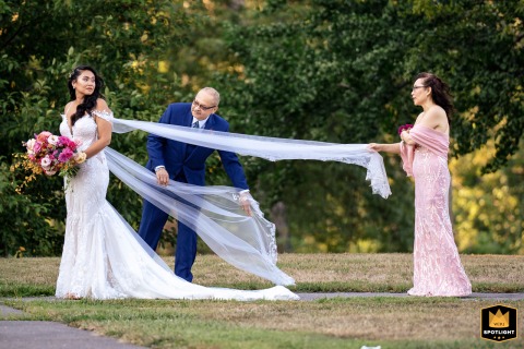 In Philadelphia, the bride's parents lovingly assist her in perfecting her wedding dress. The tender moment captures their support and care before the ceremony.